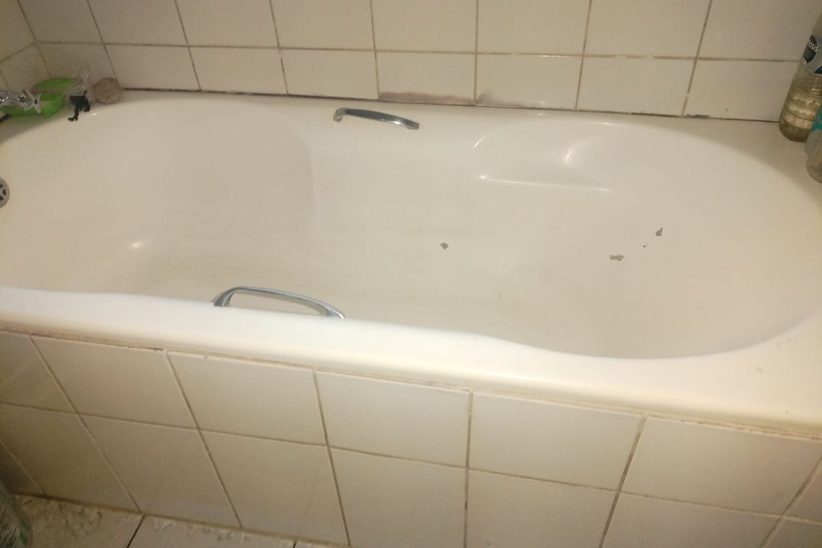 A bathroom featuring a built-in bathtub with chrome grab handles, finished with white ceramic wall and floor tiles.