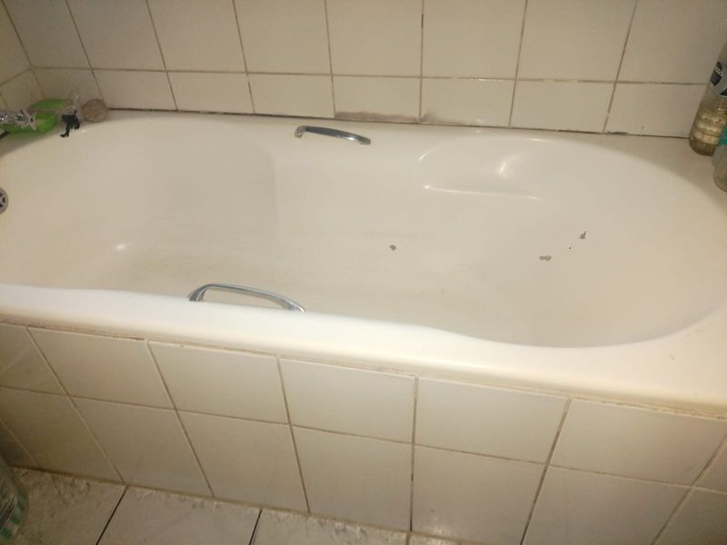 A bathroom featuring a built-in bathtub with chrome grab handles, finished with white ceramic wall and floor tiles.