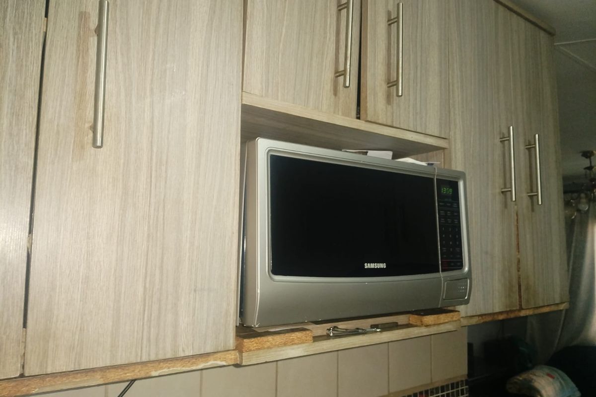 Close-up view of kitchen cabinetry featuring a built-in microwave and tiled backsplash, showing signs of wear on the cabinet edges.