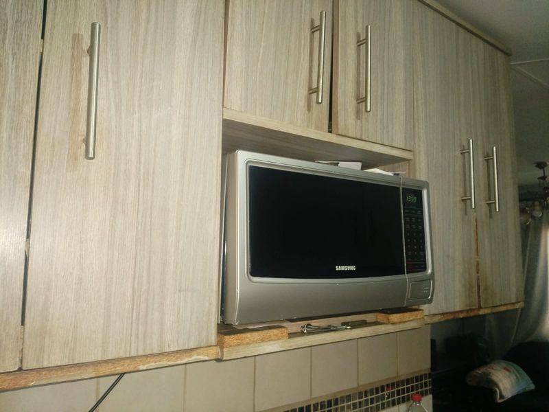 Close-up view of kitchen cabinetry featuring a built-in microwave and tiled backsplash, showing signs of wear on the cabinet edges.