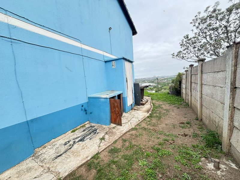 Rear exterior area featuring a concrete boundary wall, paved walkway, and a small external storage structure requiring maintenance and repair.