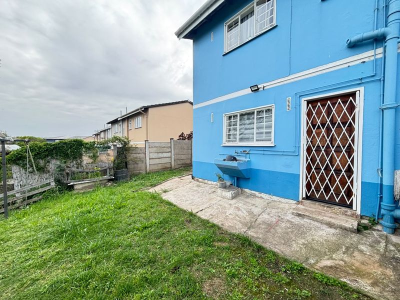 Rear exterior view of the property featuring a concrete patio, security gate, and an external wash basin against a blue painted wall.