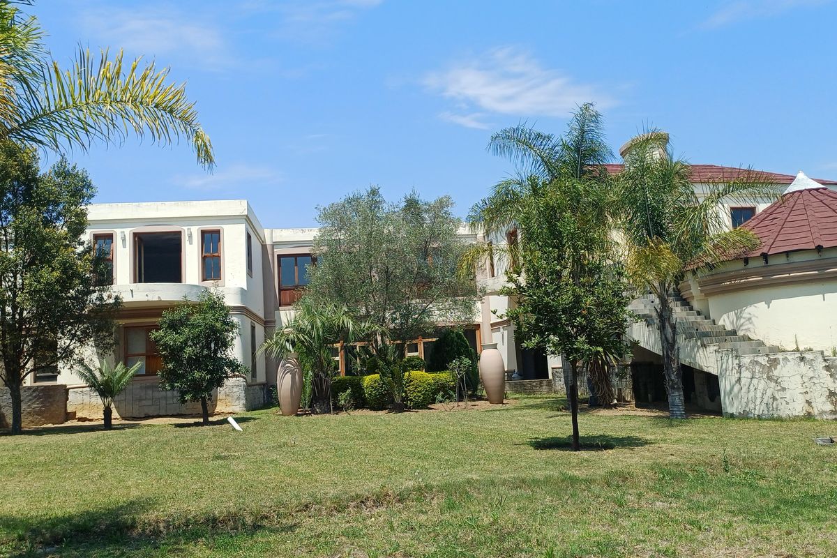 Rear view of a large multi-story residence featuring a spacious garden, tiled roof sections, and an external staircase.