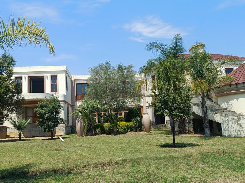 Rear view of a large multi-story residence featuring a spacious garden, tiled roof sections, and an external staircase.