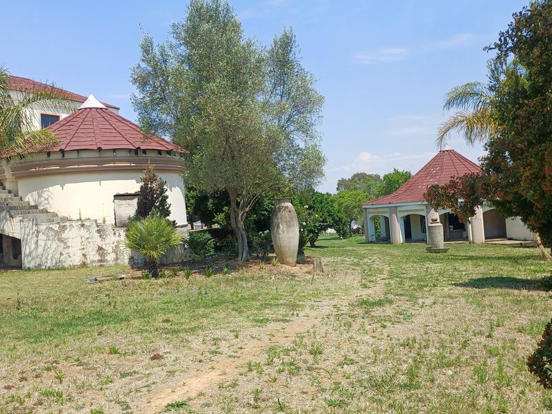 Rear view of the property featuring a unique circular structure with a tiled roof, stone staircase, and a separate covered patio area in the garden.