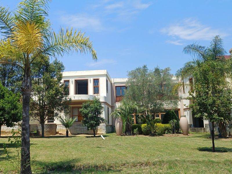 Rear view of a multi-story residence featuring stone cladding, a balcony, and an external staircase set within a spacious landscaped garden.