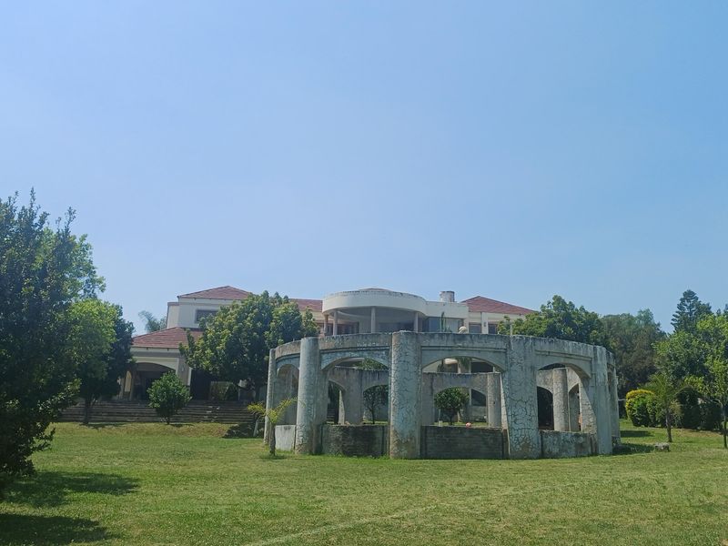 Spacious rear garden featuring a large lawn, multi-level terrace, and a weathered circular concrete gazebo structure set against the main house.