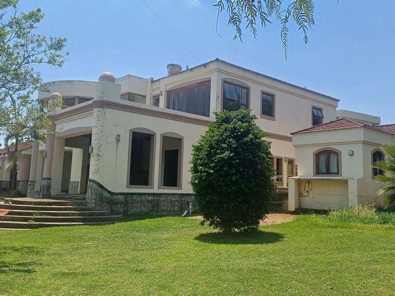 Rear view of a large multi-story residence featuring stone base detailing, concrete steps, and a covered patio area set within a spacious garden.