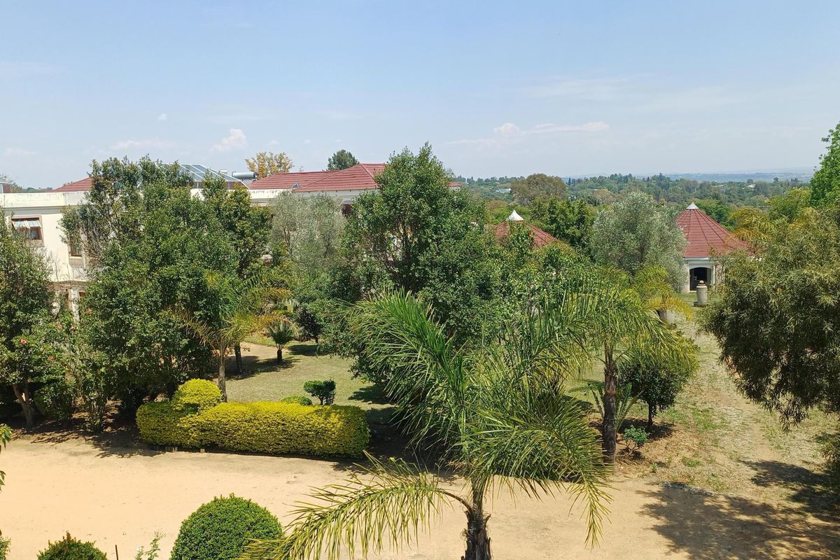 An elevated aerial view of the property grounds, showcasing the landscaped garden, mature trees, and the surrounding residential estate architecture.