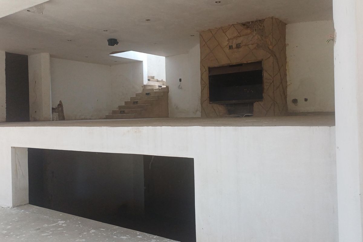 An expansive, unfinished split-level living area featuring a built-in fireplace and staircase, currently in a shell condition awaiting renovation and final finishes.
