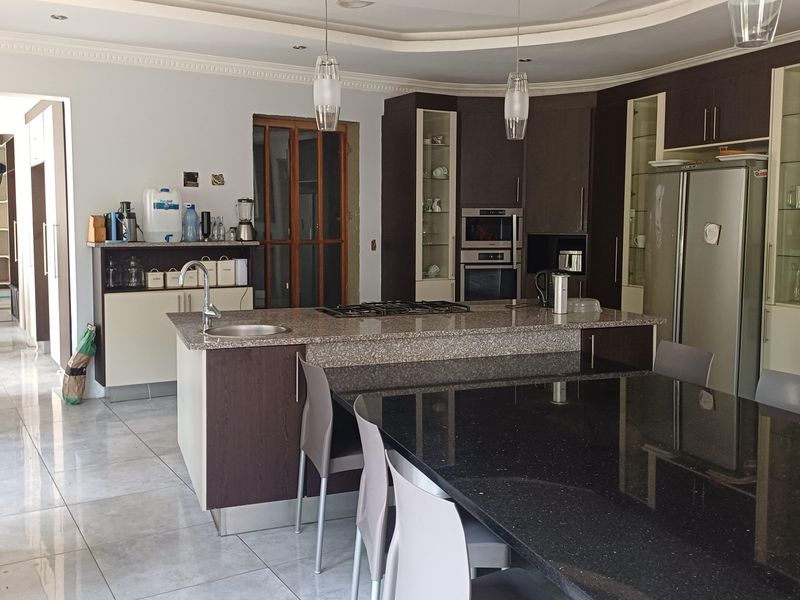 Spacious kitchen featuring a large island with granite countertops, built-in appliances, and ample cabinetry, with an adjacent dining area and tiled flooring throughout.