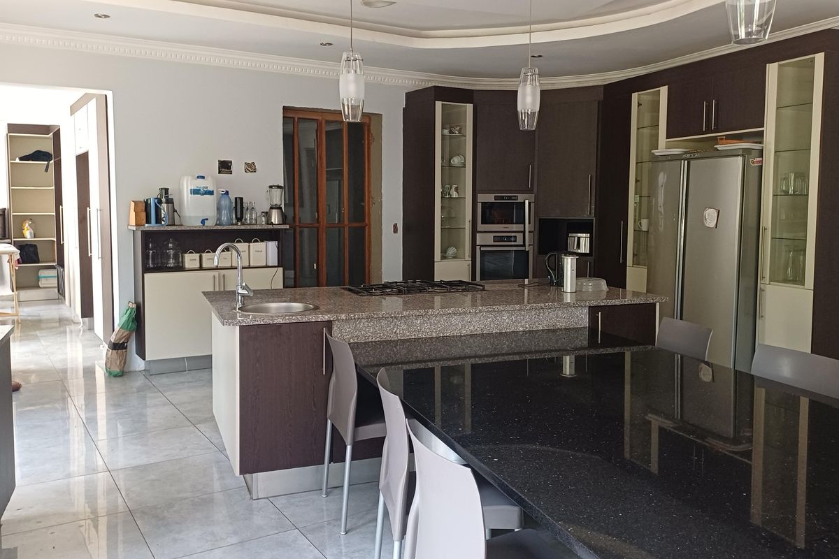 Spacious kitchen featuring a large island with granite countertops, built-in appliances, and ample cabinetry, with an adjacent dining area and tiled flooring throughout.