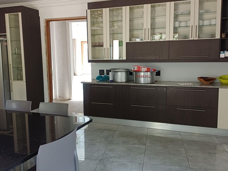 A kitchen featuring dark and light cabinetry, stone countertops, and tiled flooring, with an adjacent unfinished doorway leading to another area.