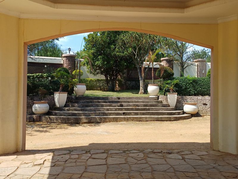 A covered patio area featuring stone paving and concrete steps leading to a landscaped garden with a stone retaining wall.