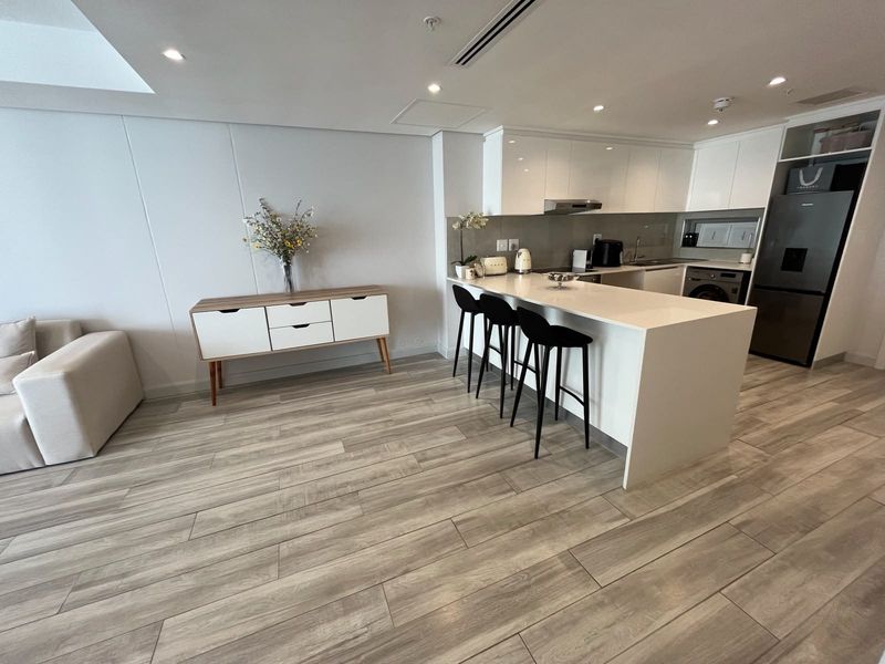 Modern open-plan living area featuring a sleek kitchen with a central island, quartz countertops, and high-quality wood-look tile flooring throughout.