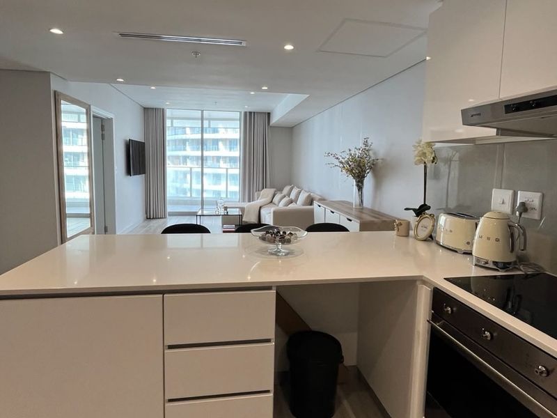 Modern open-plan apartment featuring a sleek kitchen with quartz countertops, integrated appliances, and a seamless flow to the bright living area and balcony.