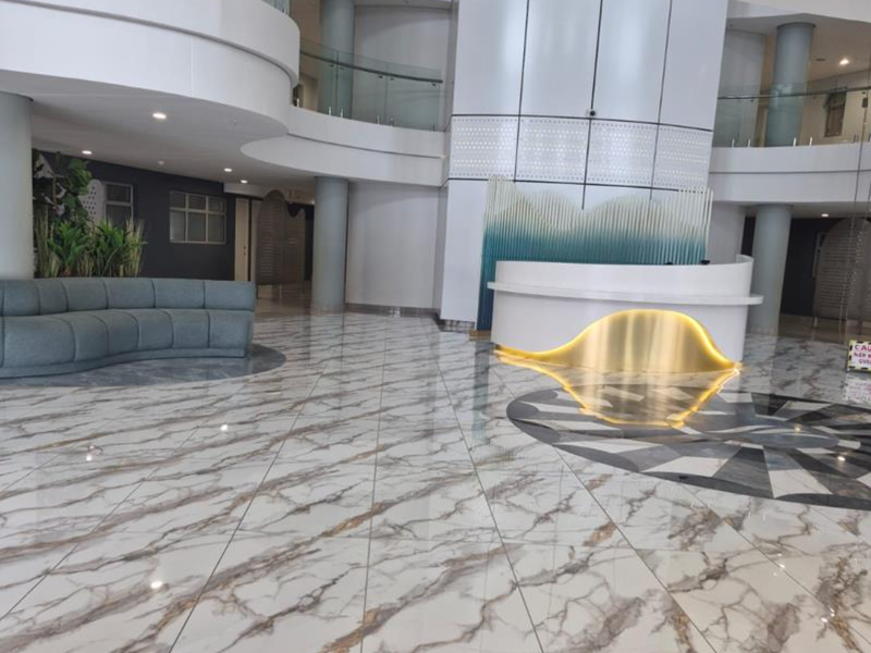 Spacious modern apartment building lobby featuring high-gloss marble-look tiled flooring, a contemporary reception desk, and an elegant mezzanine level with glass balustrades.