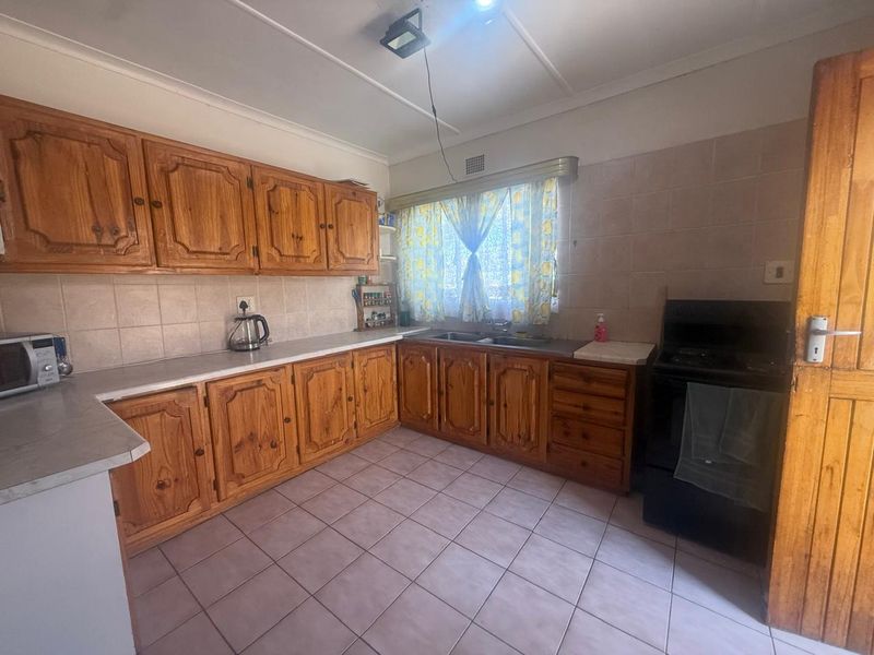 A functional kitchen featuring traditional wooden cabinetry, tiled flooring, and a double basin sink, offering a classic layout with potential for modern updates.