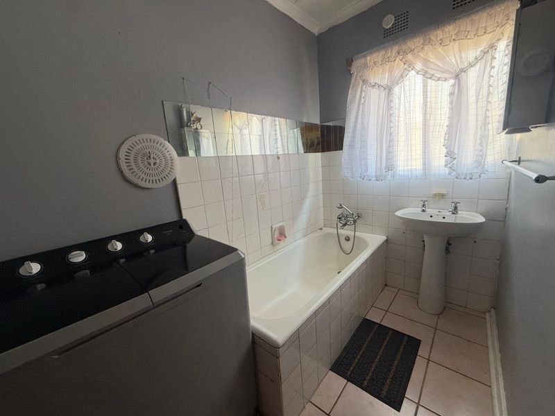 A functional bathroom featuring a pedestal basin and a built-in bathtub with tiled splashbacks, requiring some cosmetic updates to the finishes.