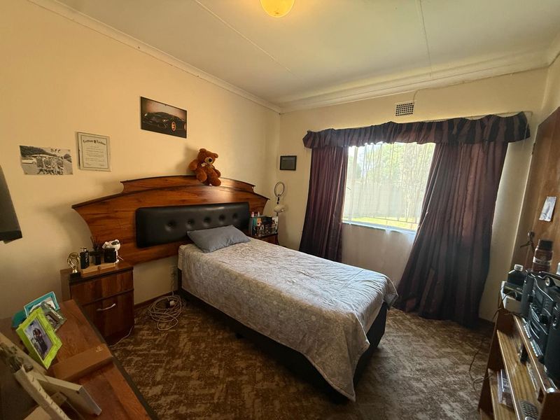 A standard bedroom featuring a built-in headboard, patterned carpeting, and a window with curtain pelmet.