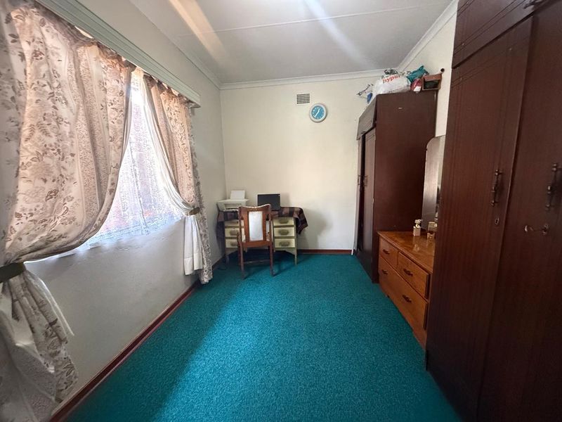 A bedroom featuring built-in cupboards, carpeted flooring, and a window with curtains, offering a functional space with potential for modernization.