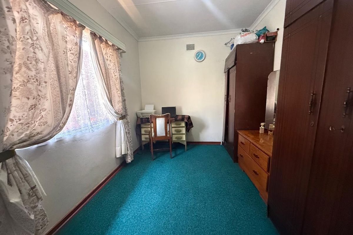 A bedroom featuring built-in cupboards, carpeted flooring, and a window with curtains, offering a functional space with potential for modernization.