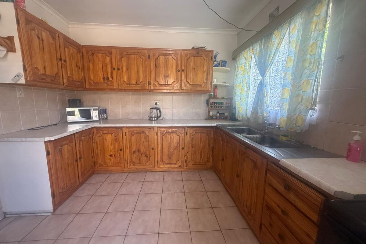 A functional kitchen featuring traditional wooden cabinetry, laminate countertops, and a double stainless steel sink with tiled flooring and backsplash.
