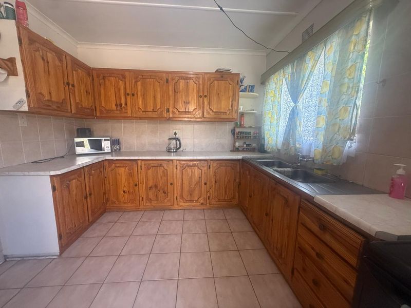 A functional kitchen featuring traditional wooden cabinetry, laminate countertops, and a double stainless steel sink with tiled flooring and backsplash.