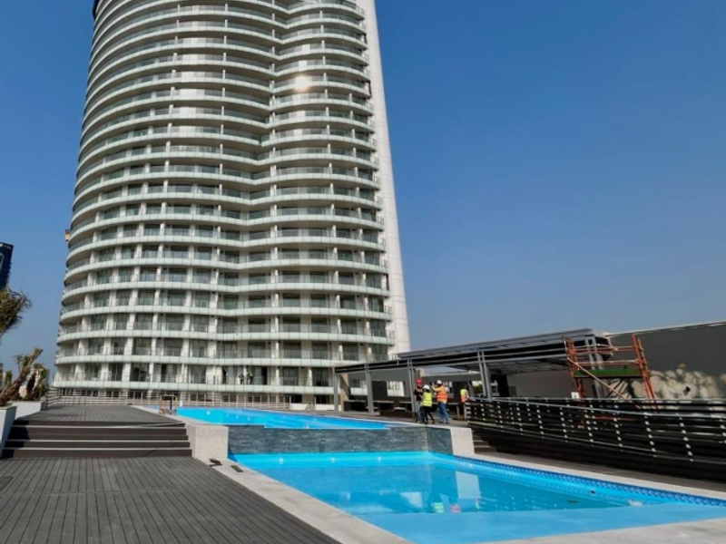 Modern high-rise apartment building featuring a sleek swimming pool area with timber decking and glass balcony railings.