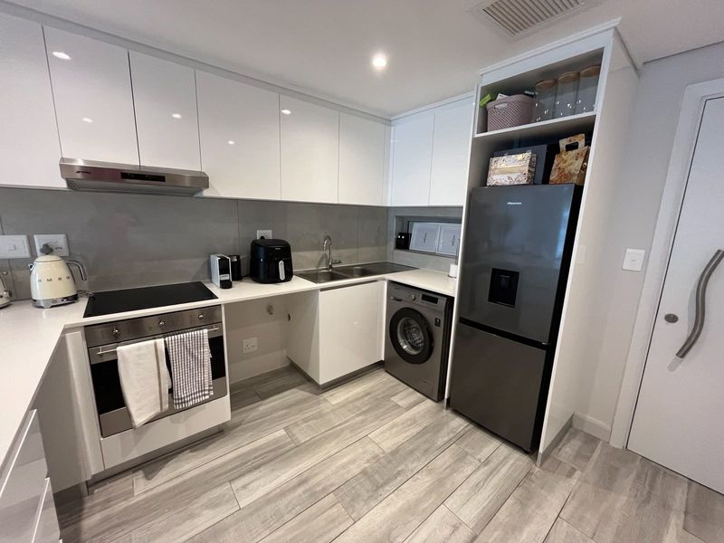 Modern kitchen featuring sleek white cabinetry, stone countertops, integrated appliances, and high-quality finishes throughout.