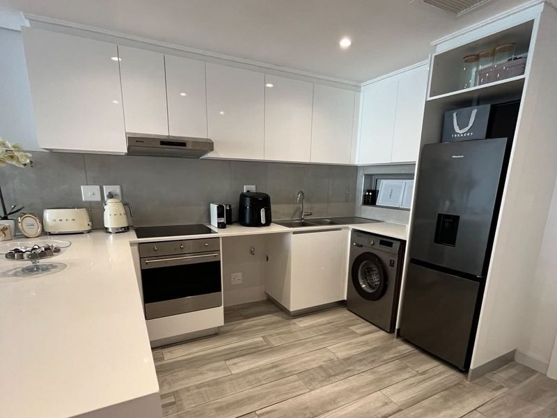 Modern kitchen featuring sleek white cabinetry, stone countertops, integrated appliances, and high-quality tiled flooring in a clean, contemporary design.