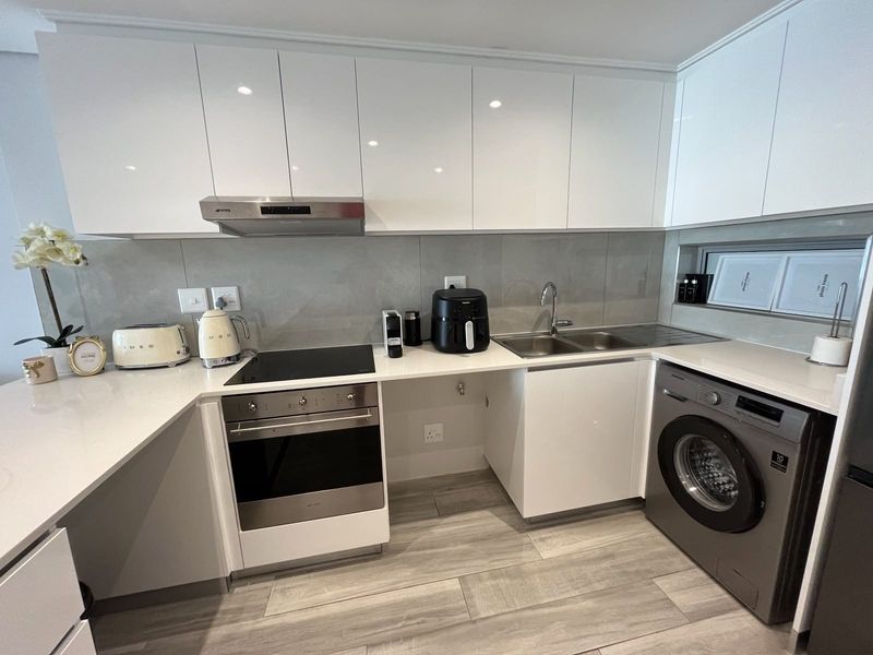 Modern kitchen featuring sleek white cabinetry, stone countertops, integrated oven and hob, and a dedicated space for a washing machine.