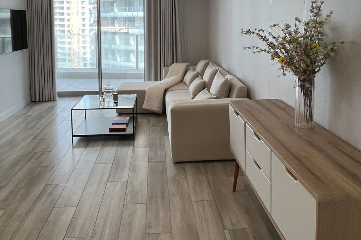 Modern living room featuring wood-look tile flooring and large sliding glass doors leading to a balcony, providing ample natural light.