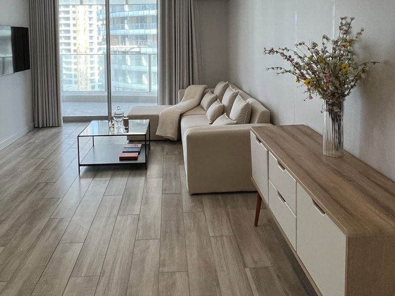 Modern living room featuring wood-look tile flooring and large sliding glass doors leading to a balcony, providing ample natural light.