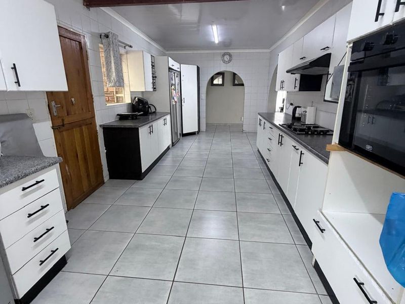 A galley-style kitchen featuring white cabinetry, dark granite countertops, built-in oven, gas hob, and tiled flooring with an arched transition to the adjacent space.