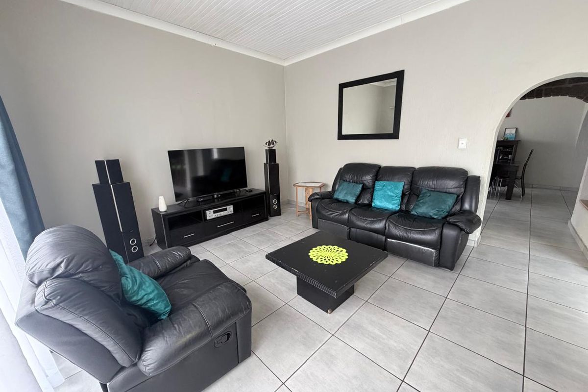 A living room featuring tiled flooring, a distinctive arched doorway leading to an adjacent space, and a white tongue and groove ceiling.