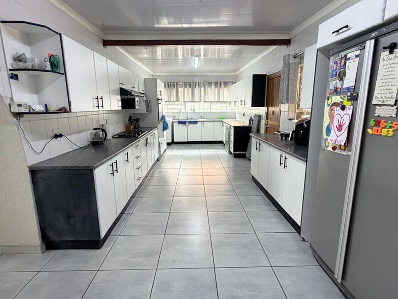 Spacious galley-style kitchen featuring white cabinetry, dark countertops, tiled flooring, and integrated cooking appliances, offering a functional and well-lit workspace.