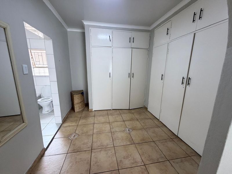 A bedroom featuring extensive built-in storage cupboards, tiled flooring, and direct access to an en-suite bathroom.
