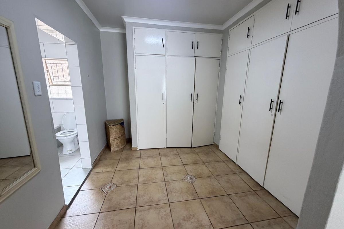 A bedroom featuring extensive built-in storage cupboards, tiled flooring, and direct access to an en-suite bathroom.