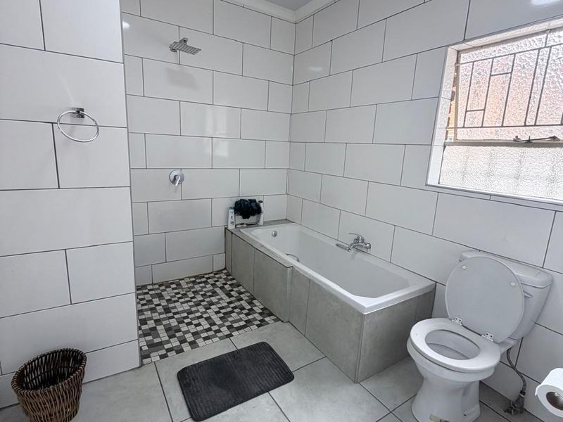 A clean, modern bathroom featuring white subway-style wall tiles, a built-in bathtub with a shower head, and a standard toilet.