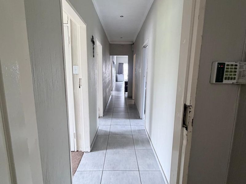 A long, tiled hallway featuring recessed downlighting and a wall-mounted security alarm keypad, providing access to multiple rooms within the home.