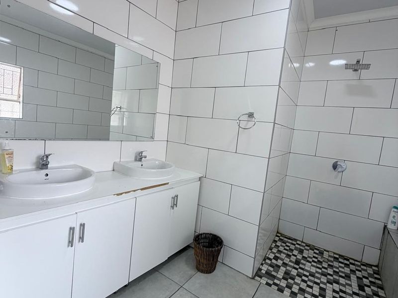 Modern bathroom featuring a double vanity with built-in cabinetry, a walk-in shower with tiled finishes, and a large wall-mounted mirror.