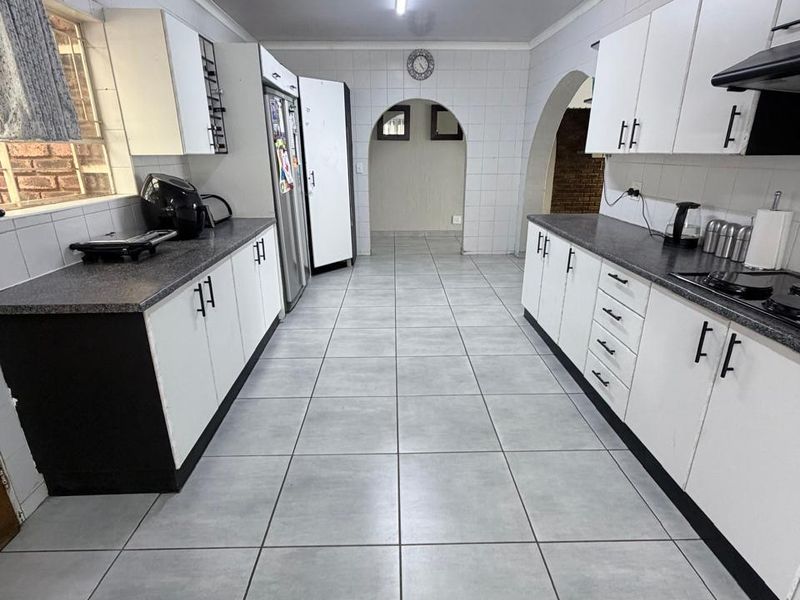 A functional galley-style kitchen featuring white cabinetry, dark laminate countertops, and tiled flooring, leading through an archway to an adjacent living space.