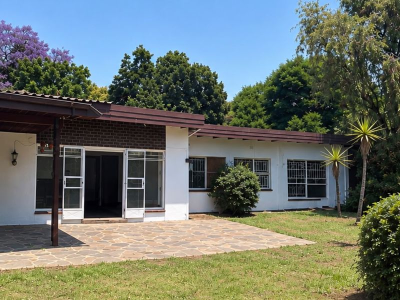 Rear view of the house featuring a stone-paved covered patio, white exterior walls with brick accents, and security-fitted windows overlooking the garden.