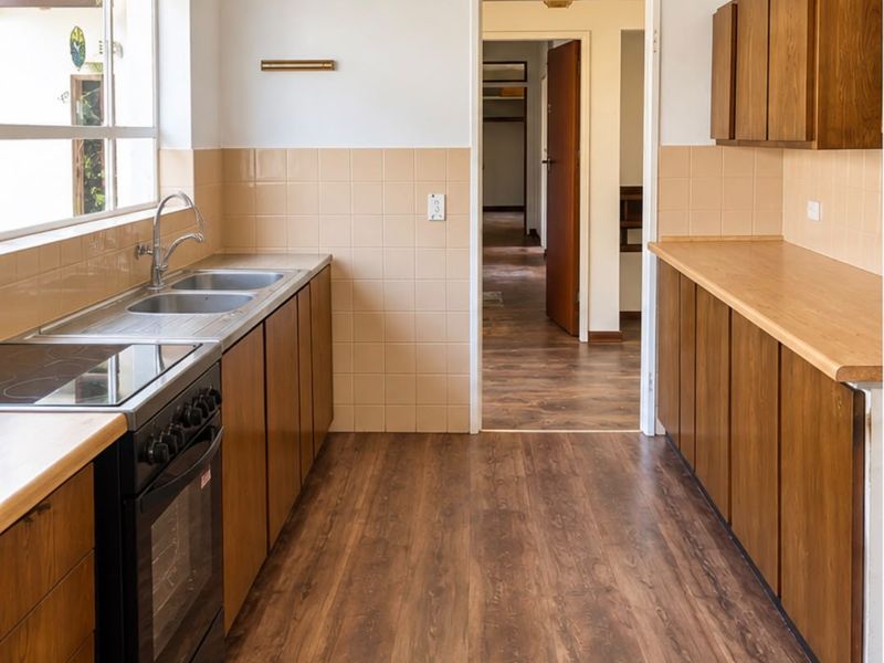 A functional galley-style kitchen featuring wooden cabinetry, laminate countertops, a stainless steel double sink, and a freestanding electric stove with tiled splashbacks.