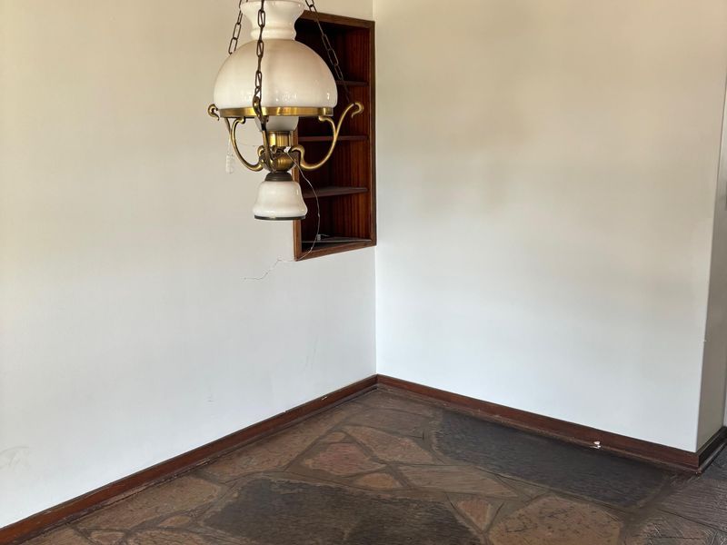 An empty living area featuring rustic flagstone flooring, a timber-paneled ceiling, and a built-in wall shelf unit.