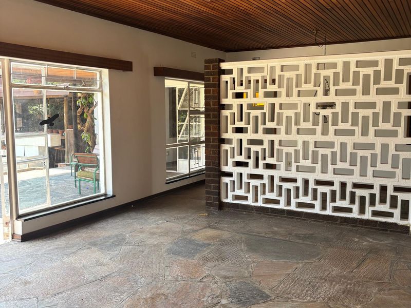 Spacious living area featuring a unique timber slat ceiling, decorative breeze block partition wall, and rustic flagstone flooring with large windows.