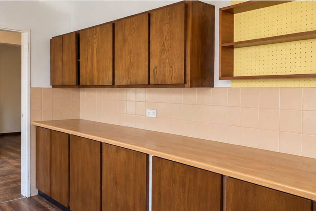 A functional kitchen area featuring traditional wooden cabinetry, a tiled splashback, and ample laminate countertop space, ready for a modern update.
