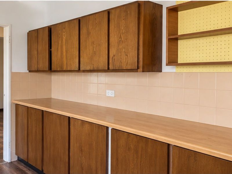 A functional kitchen area featuring traditional wooden cabinetry, a tiled splashback, and ample laminate countertop space, ready for a modern update.