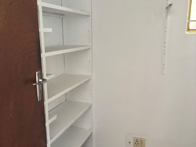 A small utility or storage space featuring built-in shelving, laminate flooring, and a timber door, requiring minor cosmetic finishing to the floor and wall edges.